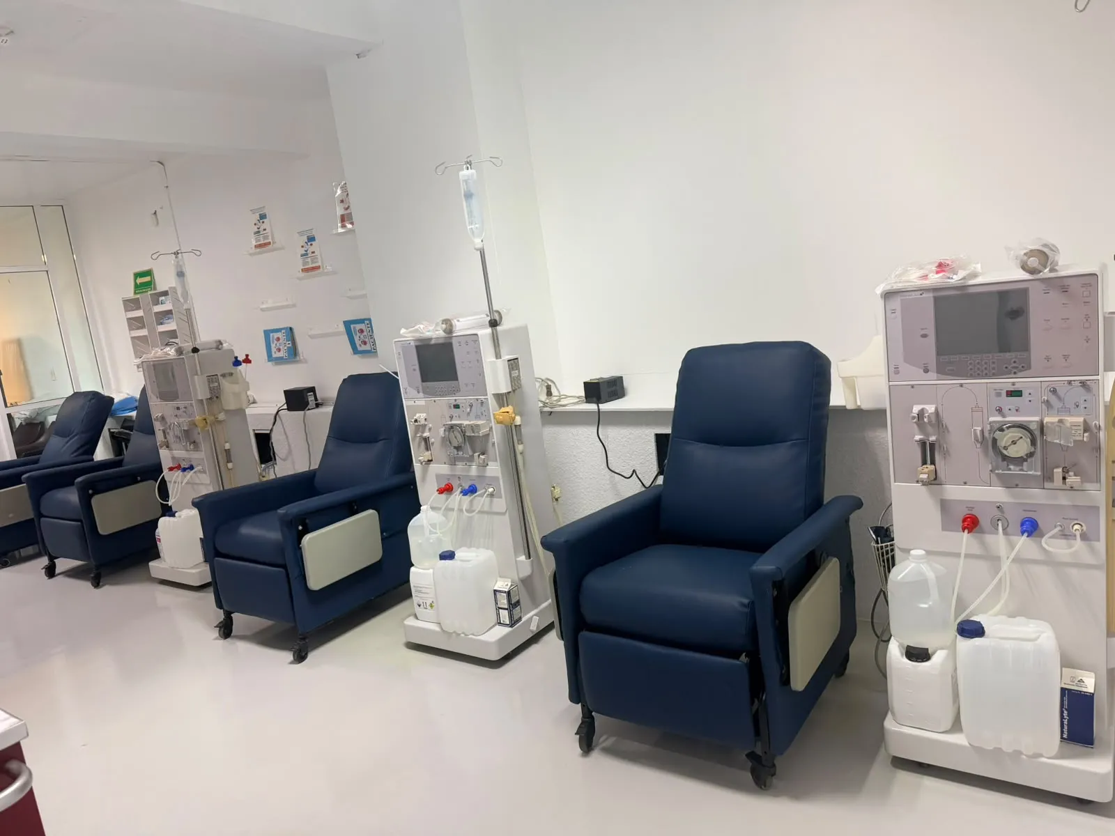 Sala de hemodiálisis de la clínica: sillones reclinables azules junto a máquinas de hemodiálisis.